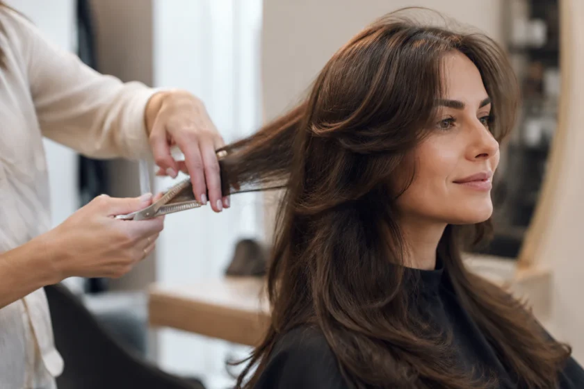 Stylist carefully thinning a woman’s thick hair with texturizing shears in a modern salon